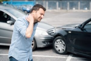 Man stands in the road and holds neck in pain in front of collided cars after an accident.